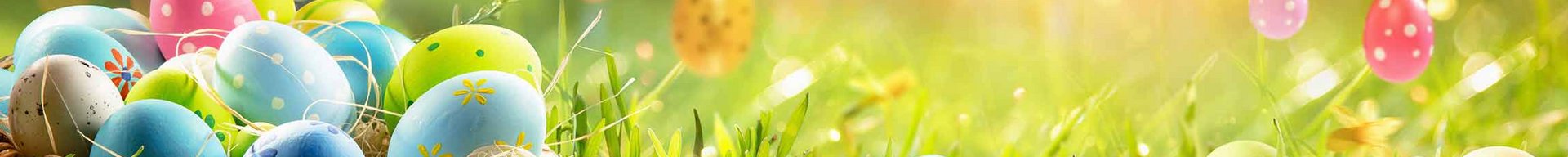 Et kurv fyldt med farverige påskeæg står på frodig grøn græs, omgivet af blomster og sollys. Et par dekorerede æg hænger fra grene i baggrunden. Bildet formidler en festlig og glædelig påskestemning.